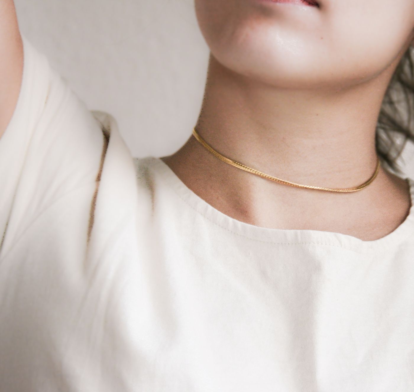 Close-up of a delicate gold chain necklace worn with an ivory top