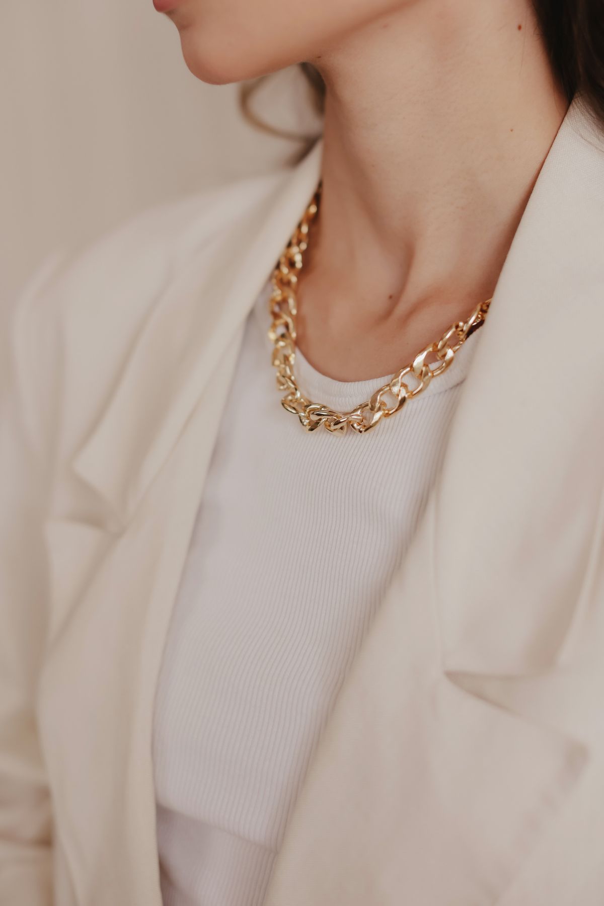 Gold curb-chain necklace worn with a cream blazer